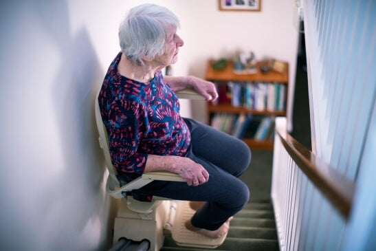 Elderly woman seated on a second hand stairlift inside a residential home.