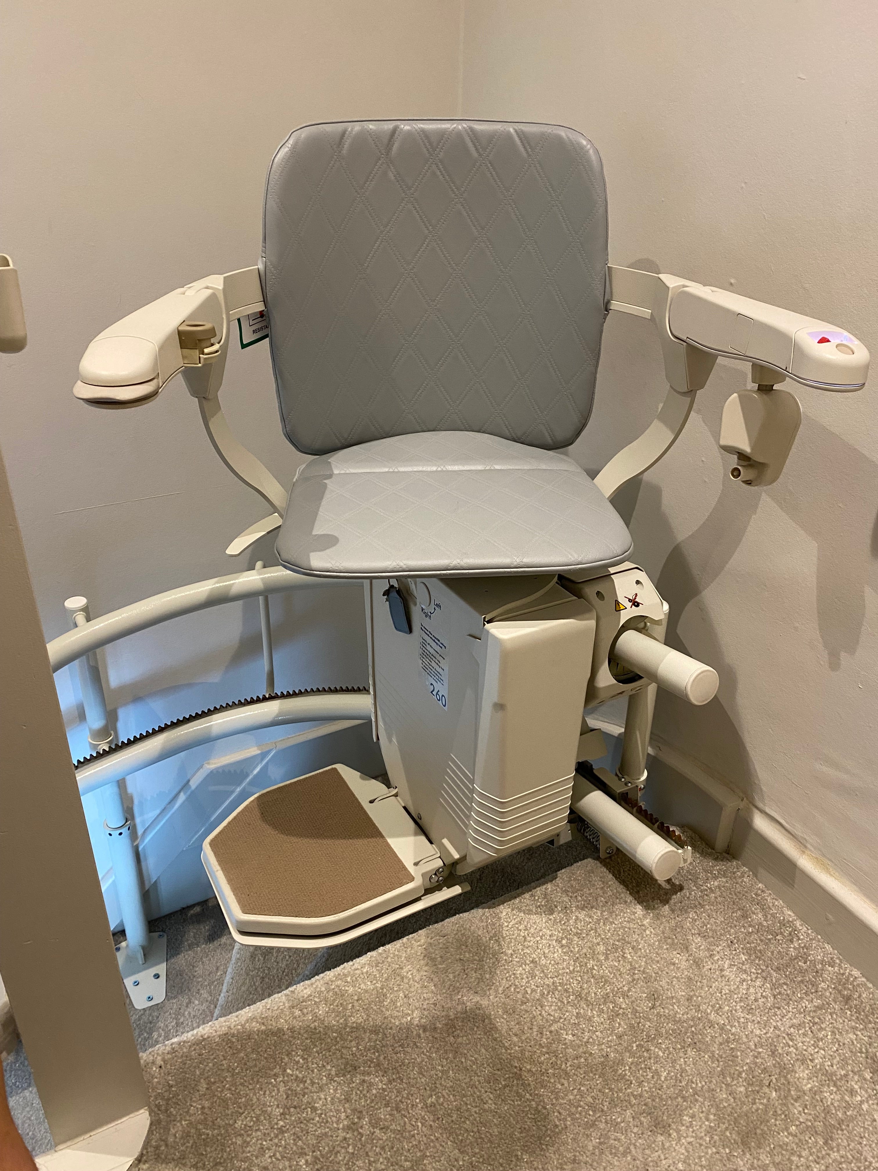 Used stairlift with gray cushioned seat and beige backrest on a concrete floor.
