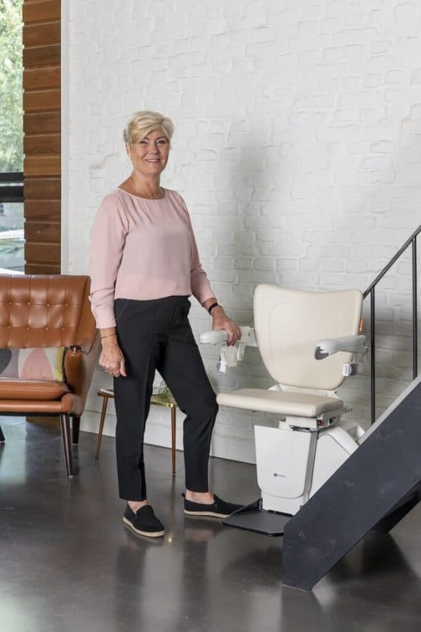 A woman stands next to her Handicare 1100 Stairlift